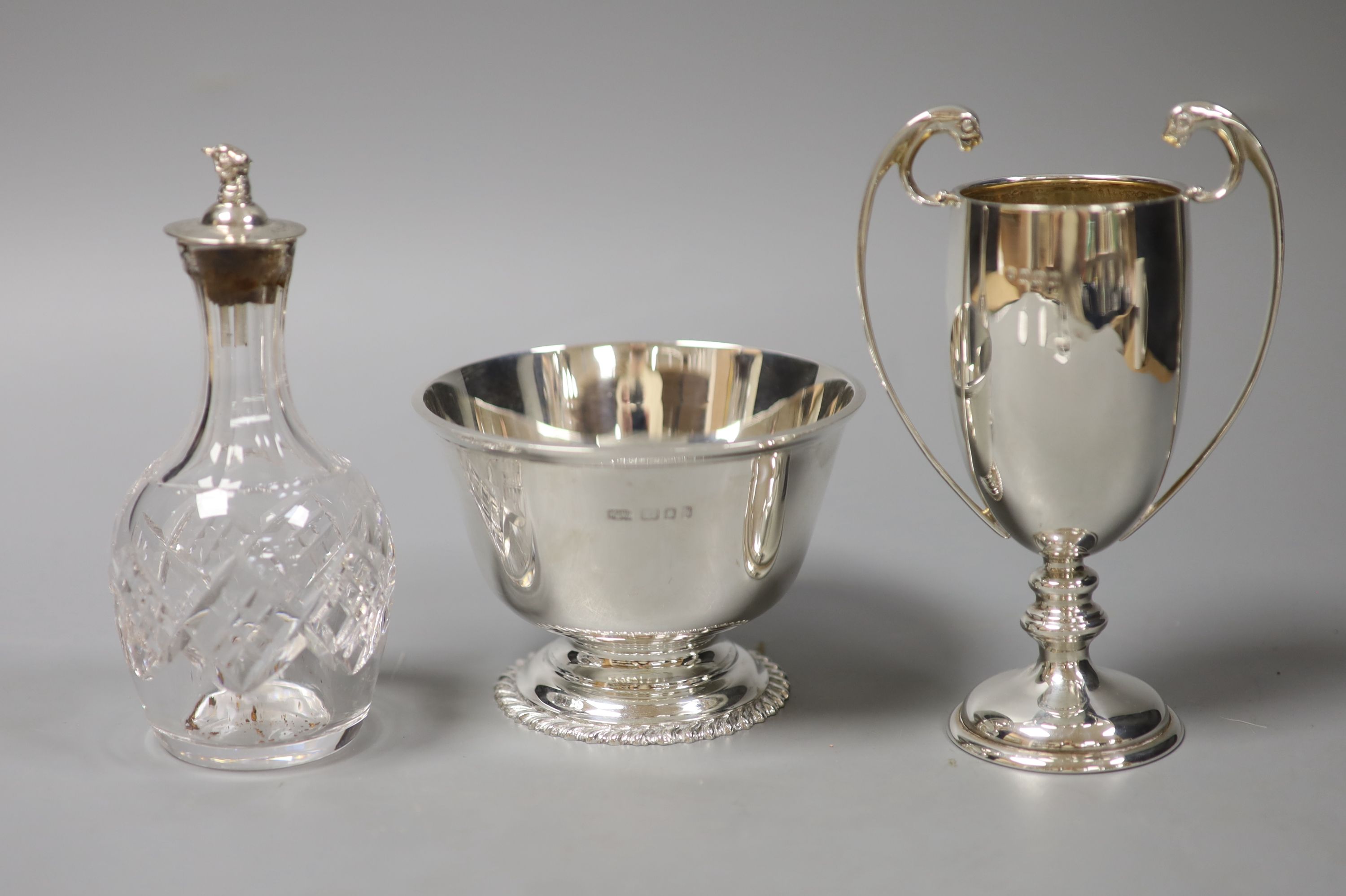 A small circular silver footed bowl, a two-handled silver trophy cup and a cut glass bottle